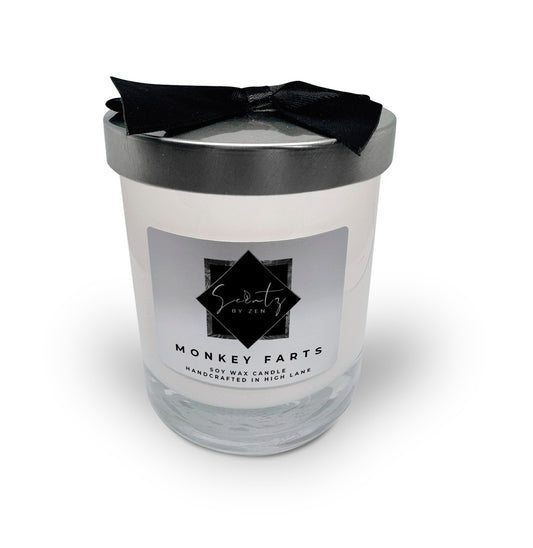 7oz White soy wax candle in a glass jar, labeled "Monkey Farts" topped with a silver lid and black ribbon, handcrafted in High Lane.